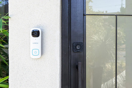 Smart doorbell attached to a house exterior next to a glass door.